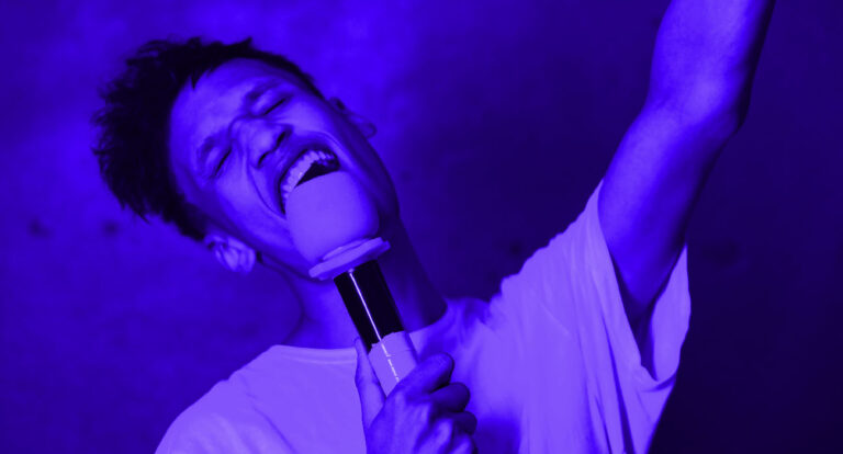 Pessoa sorrindo enquanto canta em um microfone profissional.