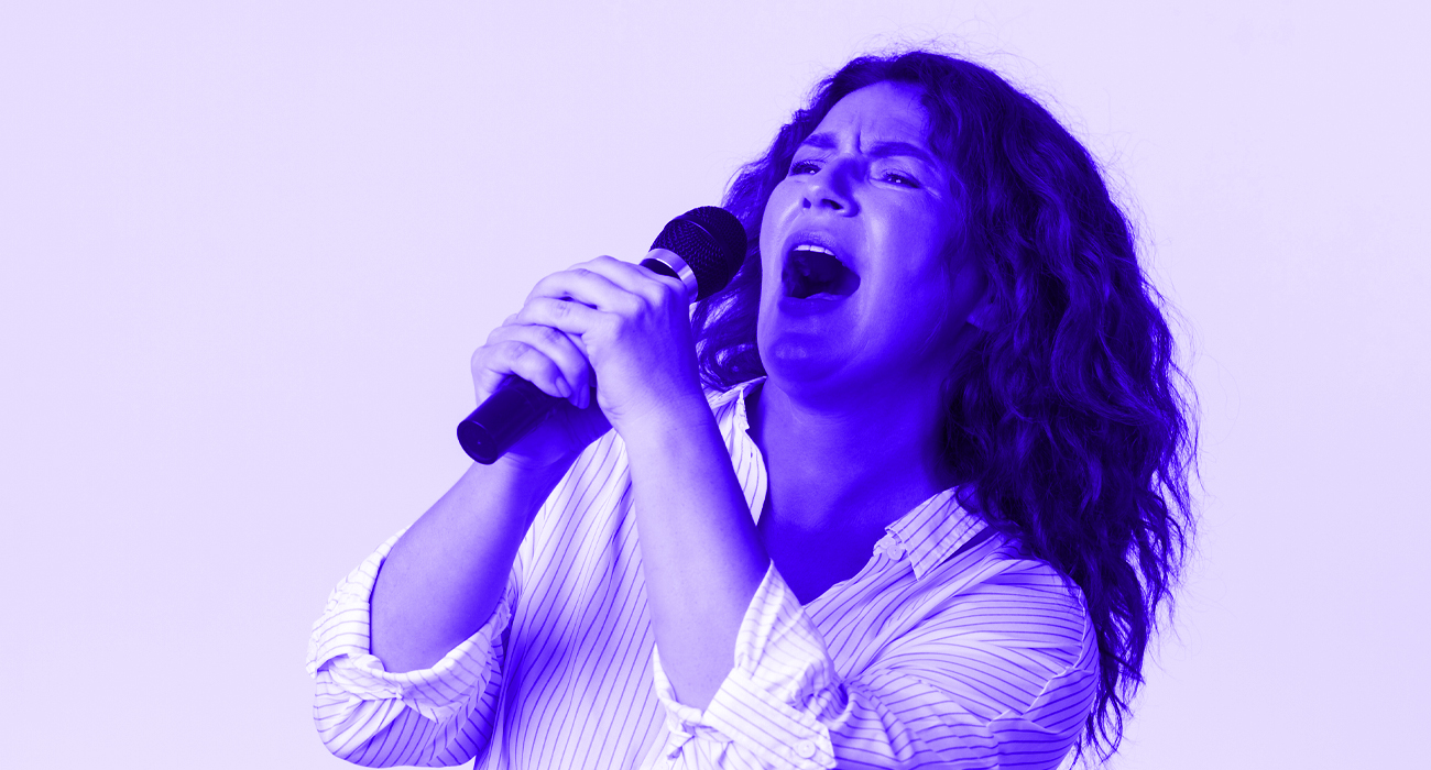 Mulher cantando com entusiasmo em um microfone de mão prateado sobre um fundo branco isolado.